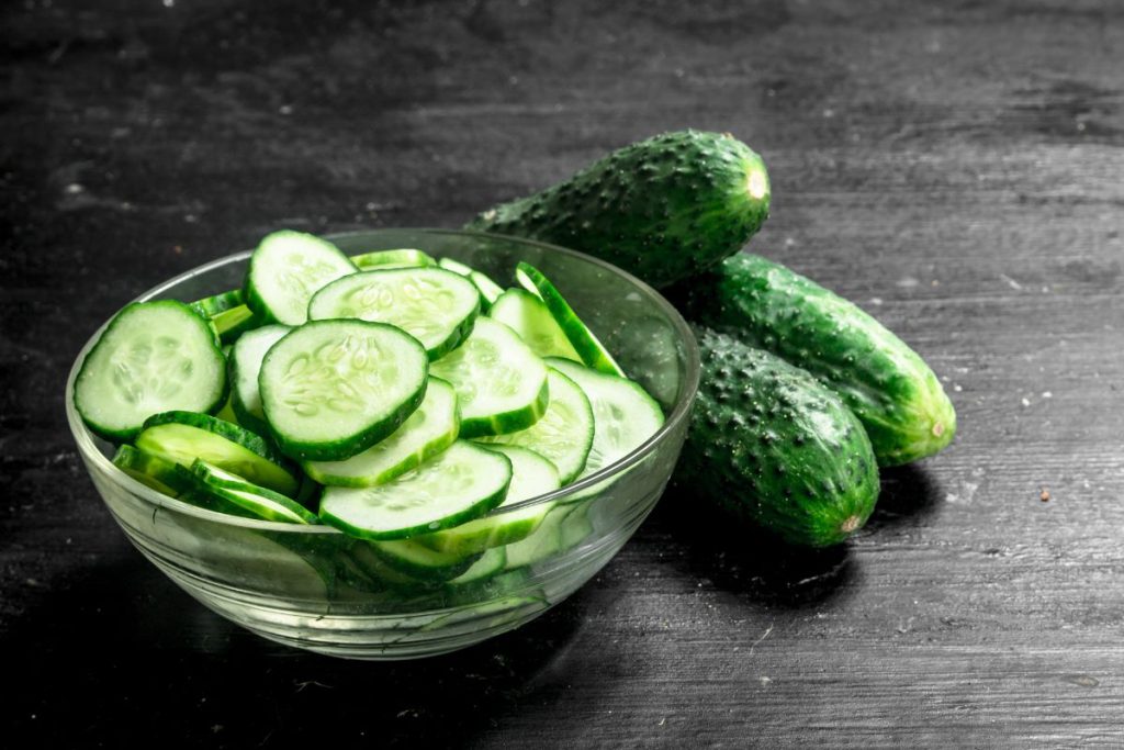 bowl of thinly sliced cucumbers next to full cucumbers for scale.