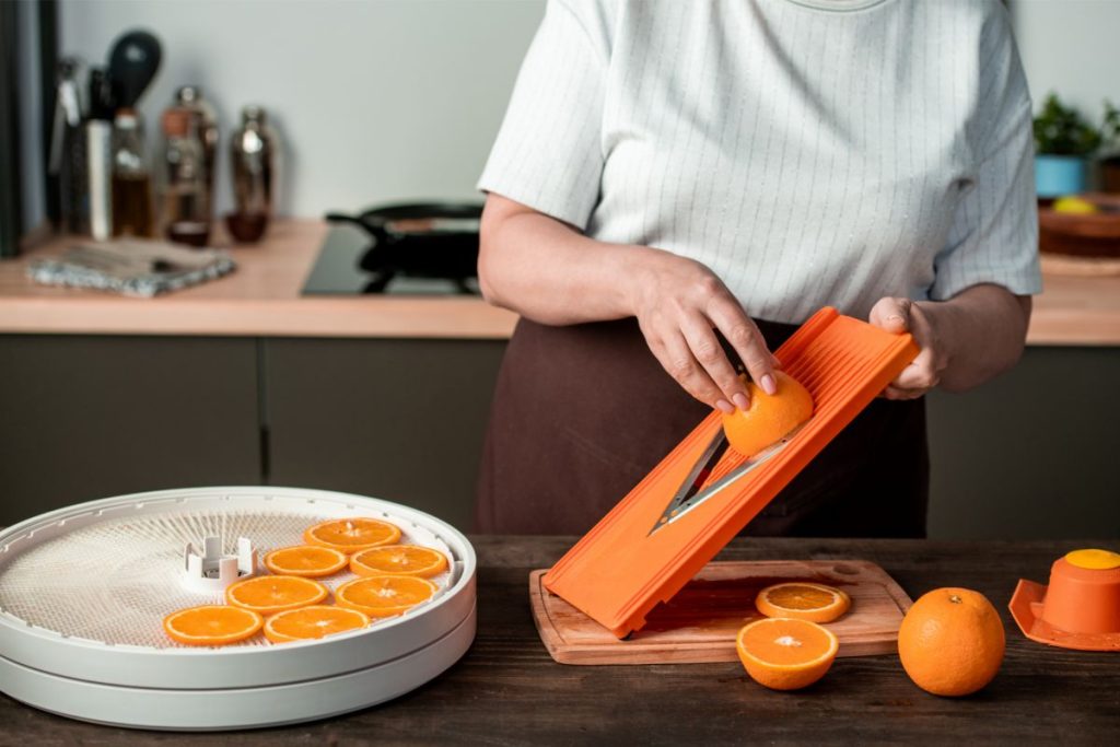 Woman slicing oranges using a mandolin and placing them in food dehydrator tray