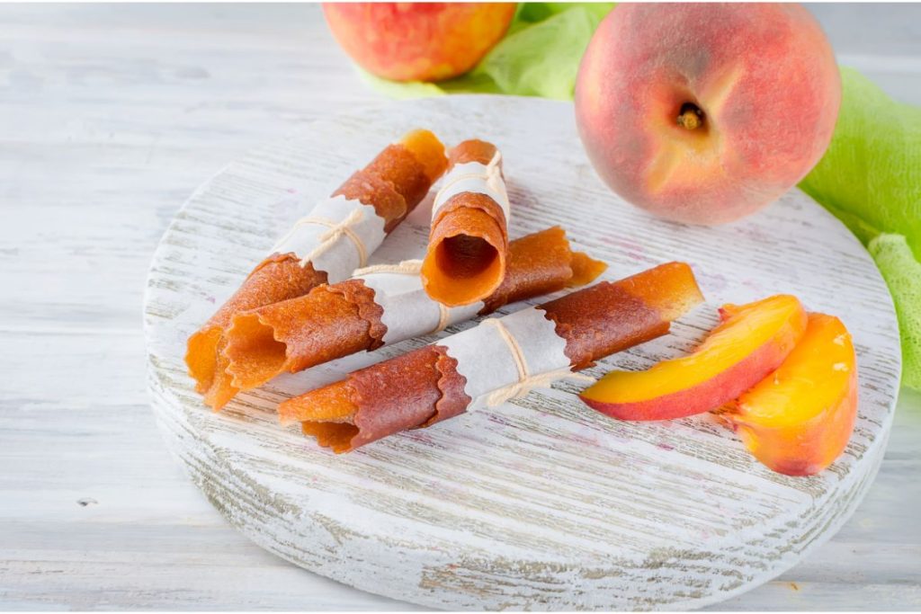 Peach fruit leather rolled up next to fresh sliced peaches