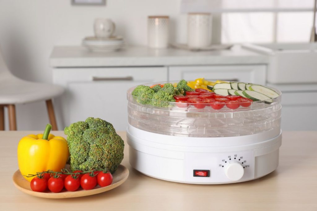 vegetables inside a food dehydrator including tomatoes yellow bell pepper and broccoli