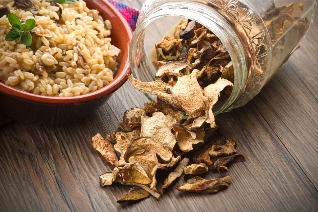 Dried porcini mushrooms next to a bowl of rice with rehydrated porcinis