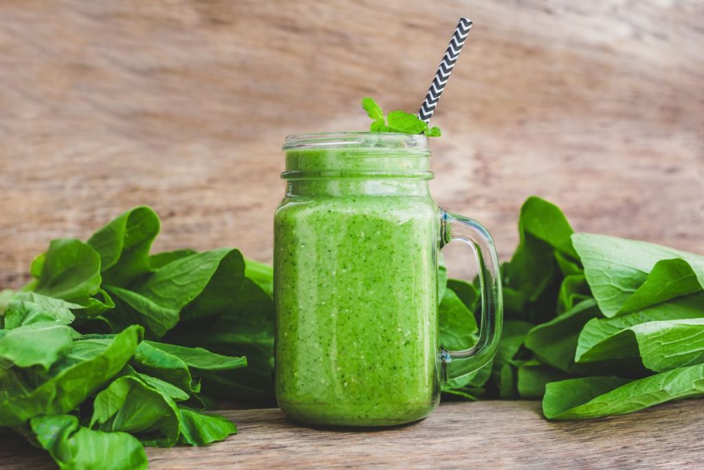 spinach smoothie next to fresh spinach leaves
