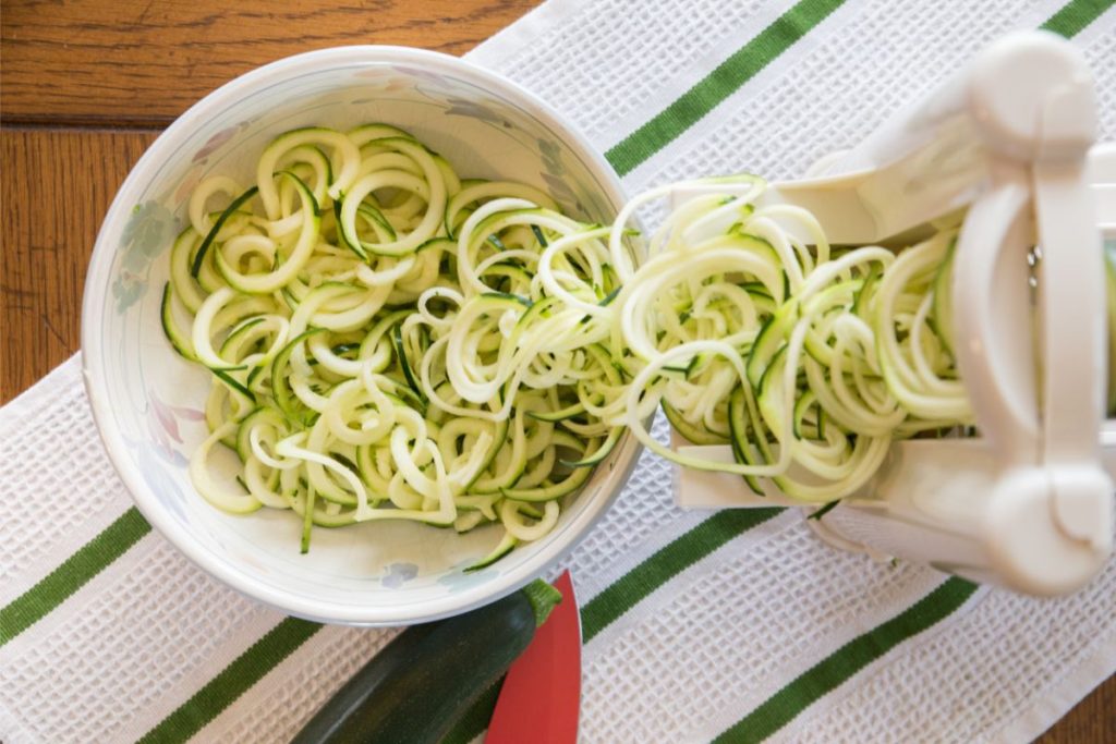 Spiralizer machine with zucchini strings coming out of it into a bowl