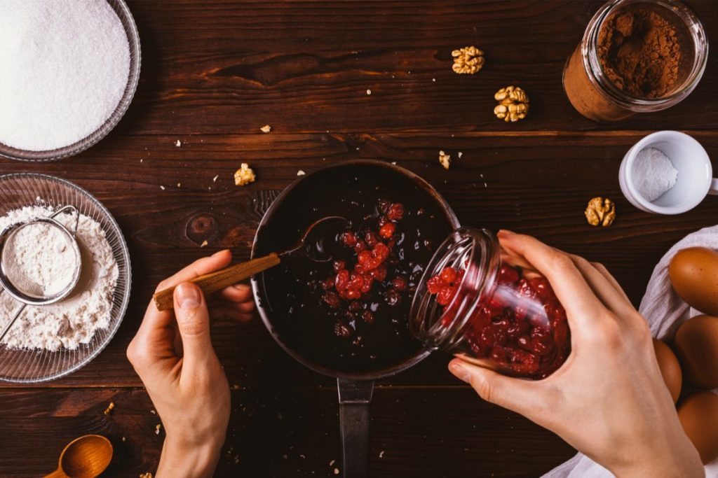 Woman pouring dried cherries into a pot surrounded by baking ingredients