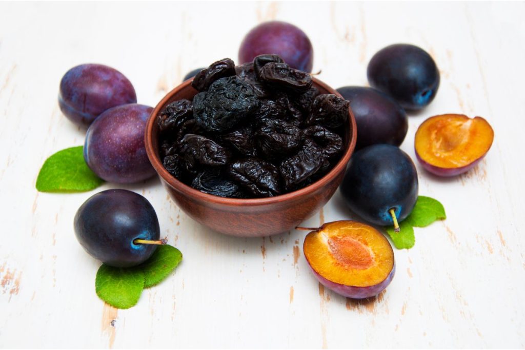 Fresh plums surrounding a bowl of prunes
