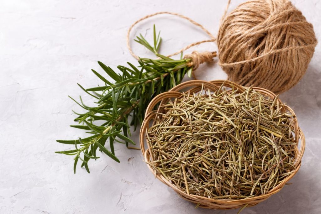 Bundle of fresh rosemary tied with twine next to a bowl of dried rosemary