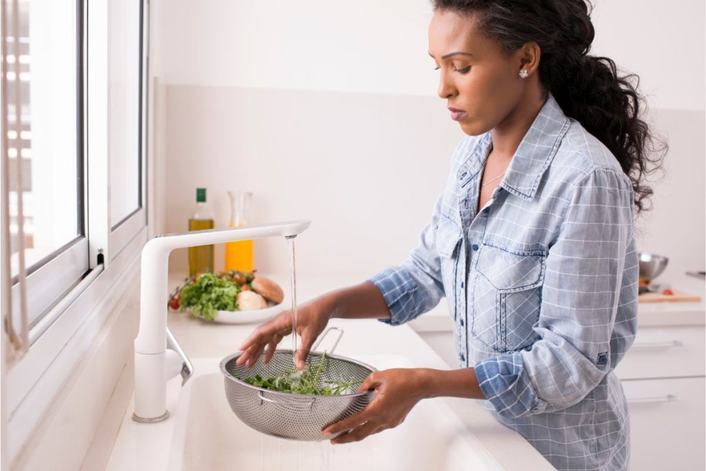 Woman rinsing herbs in colander at the sink