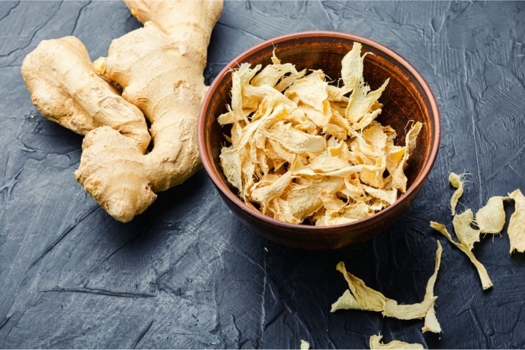 Bowl of dehydrated ginger root slices next to a whole ginger root
