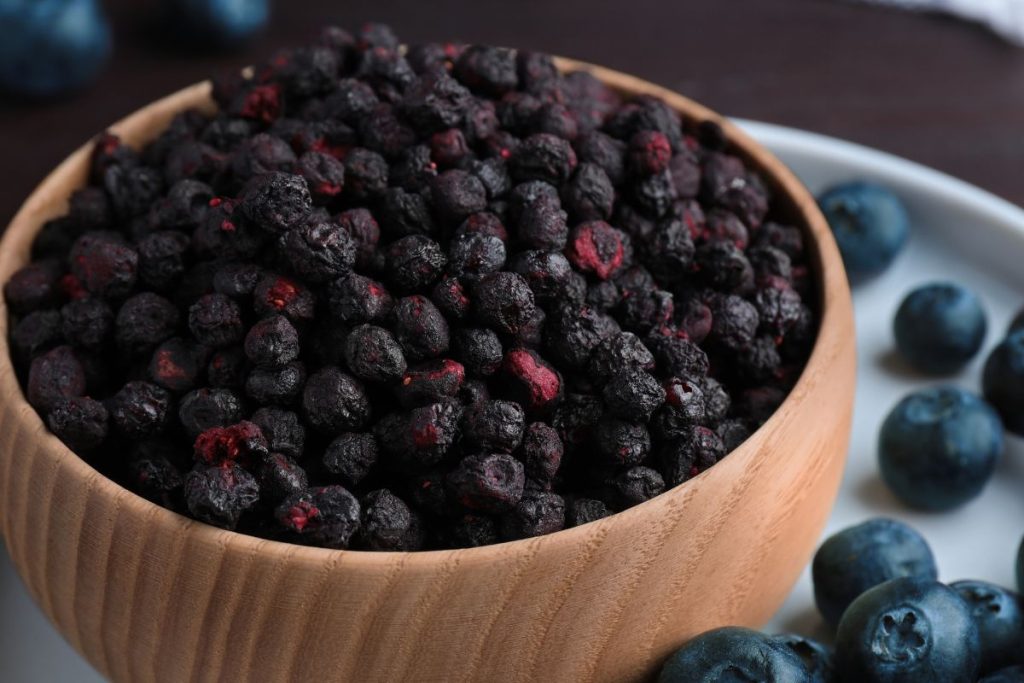 Large bowl of freeze-dried blueberries next to scattered fresh blueberries