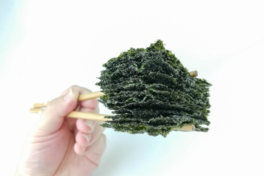 Stack of dehydrated seaweed sheets held between two chopsticks
